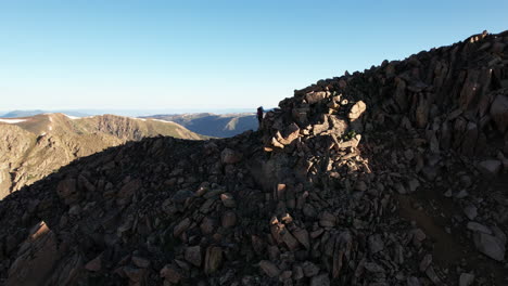 Vista-Aérea-De-Un-Excursionista-Con-Mochila-Caminando-Sobre-Una-Colina-Rocosa