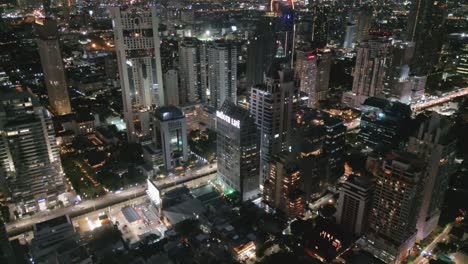 Vista-Aérea-Del-Edificio-Rascacielos-Del-Paisaje-Urbano-Iluminado-Por-La-Noche