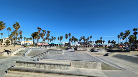 Zeitlupen-Schwenk-Von-Skateboardern-Auf-Der-Betonanlage-Des-Venice-Beach-Skateparks-In-Los-Angeles,-Kalifornien-Mit-Palmen,-Reisen,-Extremsporttourismus,-USA