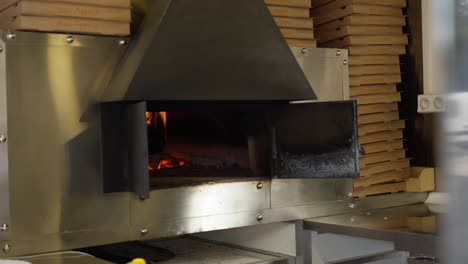 focus-on-a-large-professional-pizza-oven-with-the-flame-of-the-fire-inside,-empty-pizza-boxes-all-around