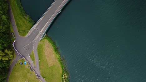 Foto-De-Ariel-De-Triatlón-En-El-Lago-Dorney,-Triatletas-En-Bicicleta-Y-Compitiendo-En-La-Pista,-Cruzando-Un-Puente-De-Agua