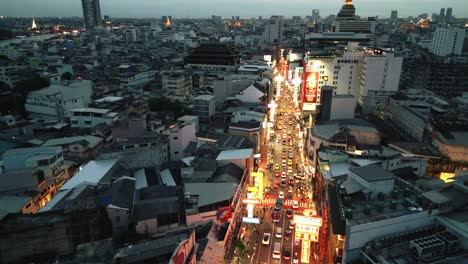 drone-fly-above-Yaowarat-road-in-Chinatown-district-illuminated-at-night-with-neon-sign-and-street-food-vendor-stalls