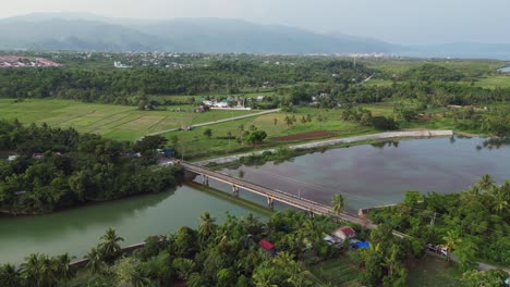 Orbiting-aerial-view-of-scenic-bridge-over-a-calm-river-in-between-quaint-Philippine-rural-area