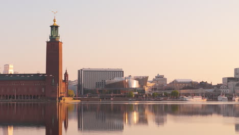 Flight-of-swans-passing-City-Hall-overlooking-Riddarfjärden-in-Stockholm,-aerial