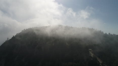 Schwenk-Drohnenaufnahme-Von-Nebel,-Der-über-Einen-Berggipfel-Zieht-Und-Auf-Einer-Leeren-Straße-Endet