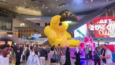 Busy-crowds-of-people-with-big-yellow-teddy-called-untitled-lamp-bear-in-Hamad-International-Airport-in-Doha,-Qatar