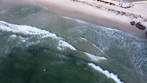 High-Aerial-view---surf-of-Indian-Ocean-and-lone-swimmer-at-Cottesloe-Beach,-WA