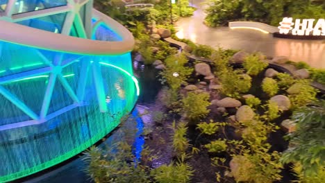 Rising-scenic-view-over-The-Orchard-rainforest-garden-of-trees,-waterfall-and-stream-in-Hamad-International-Airport-in-Doha,-Qatar