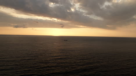 Drone-dolly-long-shot-toward-freighter-in-open-sea-during-scenic-golden-sunset