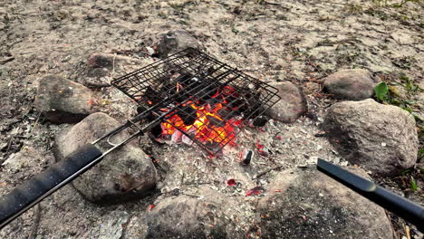 Electronic-air-blower-used-to-stoke-and-increase-heat-of-fire-with-charcoal-briquettes-around-stone-firepit-with-metal-cooking-grate