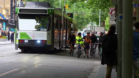 Swarms-of-cyclists-ride-in-their-dedicated-lane,-alongside-the-tram-tracks-where-trams-rumble-along,-in-Melbourne's-city,-highlighting-the-city's-the-vibrant-and-green-urban-environment