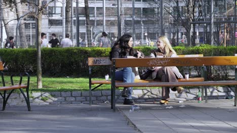 Two-friends-sitting-in-a-park-in-Vienna,-Austria,-chatting-and-smoking-cigarettes