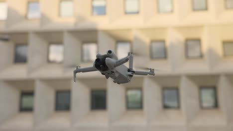 Drone-rotating-mid-air-against-a-modern-building-backdrop,-showcasing-dynamic-aerial-technology-and-urban-environment