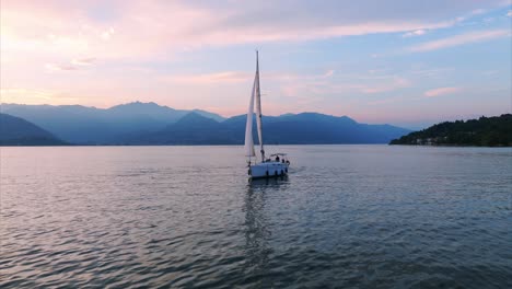 Aerial-video-of-a-sailboat-on-calm-waters-at-sunset,-with-a-circular-camera-rotation-capturing-the-scenic-landscape-and-serene-atmosphere