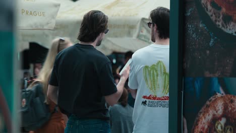 Two-men-standing-under-umbrellas,-seen-from-behind,-at-Zagreb's-Cest-is-d'Best-street-festival