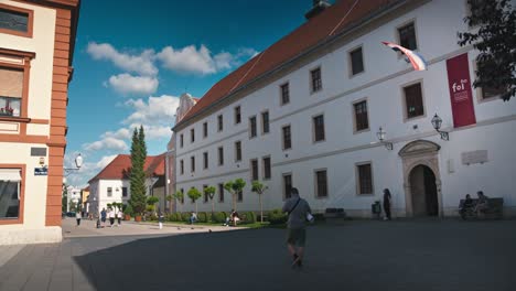 Día-Soleado-En-Varaždin,-Croacia,-Con-Un-Edificio-Histórico-Con-Una-Bandera-Croata,-Un-Entorno-Bien-Mantenido-Y-Gente-Caminando-Por-La-Zona.