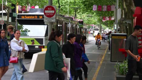 Los-Tranvías-Se-Detuvieron-En-La-Parada-De-Tranvía-De-Swanston-Street-Con-Peatones-Cruzando,-Escena-De-La-Calle-Capturada-Durante-La-Hora-Pico-En-El-Bullicioso-Distrito-Central-De-Negocios-De-La-Ciudad-De-Melbourne.