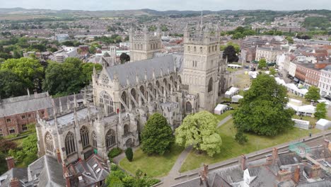 Aerial-fly-in-capturing-the-grandeur-of-Exeter-Cathedral-amidst-lush-greenery-and-historic-buildings,-Exeter,-Devon,-UK,-July-2024