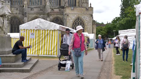 Locals-and-tourists-explore-a-bustling-local-market-with-tents-and-stalls-outside-the-Cathedral,-Exeter,-Devon,-UK,-June-2024