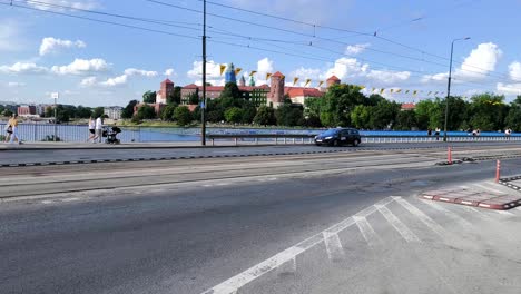 Pedestrians-and-traffic-crossing-a-bridge-with-a-clear-view-of-Wawel-Royal-Castle-in-the-background,-Krakow,-Poland