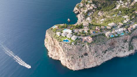 Vista-Aérea-Del-Acantilado-Mirador-De-La-Mola-Y-Barco-En-La-Bahía-De-Aguas-Turquesas,-España