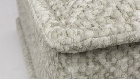 Camera-slowly-zooms-in-on-corner-of-fluffy-grey-wool-sofa-cushion-against-white-background