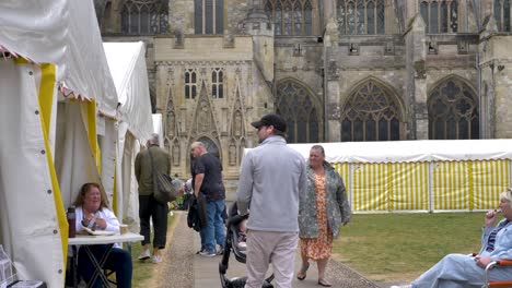 People-exploring-the-market-outside-the-city-cathedral-with-stalls-and-tents,-Exeter,-Devon,-UK,-June-2024