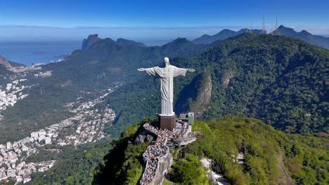 Breathtaking-aerial-footage-of-Christ-the-Redeemer-statue-in-Rio-de-Janeiro,-showcasing-the-city's-vibrant-life-and-stunning-surrounding-mountains-backdrop-under-a-clear-blue-sky