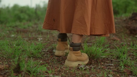 A-person-in-a-long-skirt-walking-through-a-grassy-field,-close-up