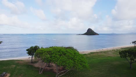 A-peaceful-morning-view-of-Mokoli'i-Island,-also-known-as-Chinaman's-Hat,-from-a-lush-green-beach-park-on-Oahu