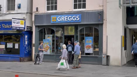 Außenansicht-Des-Greggs-Ladens-Mit-Leuten,-Die-Schlange-Stehen,-Um-Lebensmittel-Zu-Kaufen,-Exeter,-Devon,-Großbritannien,-Juli-2024