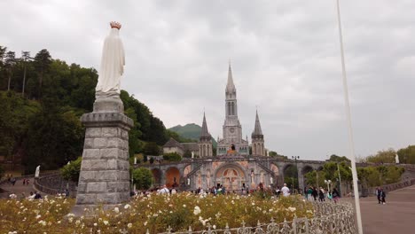 Rosenkranzplatz-Mit-Der-Gekrönten-Statue-Im-Vordergrund-Und-Dem-Heiligtum-Von-Lourdes-Im-Hintergrund