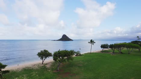 A-serene-aerial-view-of-Mokoli'i-Island,-also-known-as-Chinaman's-Hat,-from-a-lush-green-beach-park-on-Oahu