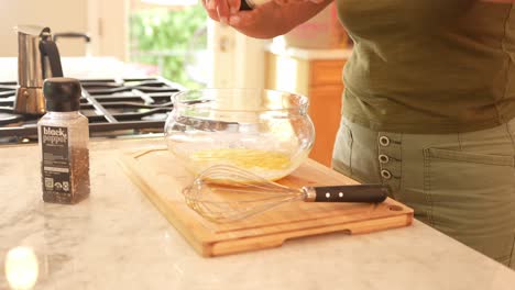 A-side-angle-of-a-woman-seasoning-eggs-with-salt-and-pepper,-then-scrambling-them-in-a-bowl-inside-a-modern-kitchen