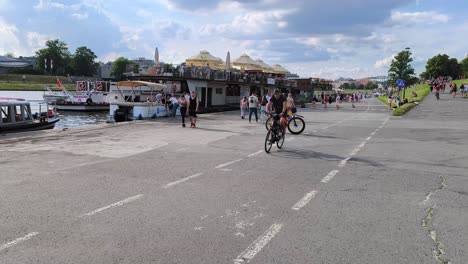 people-walking-and-cycling-along-the-Wisla-River,-with-boats-docked-and-a-vibrant-riverside-atmosphere