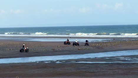 A-group-of-ATV-Quad-driving-along-the-beach-during-an-outdoor-tourist-adventure-tour-in-Bali,-Indonesia