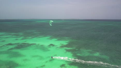 A-kite-surfer-gliding-over-vibrant-green-waters-near-crasky,-los-roques,-venezuela,-aerial-view