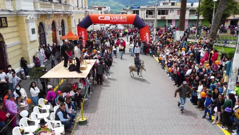 Toma-De-Drone-Del-Inicio-De-La-Tradicional-Carrera-De-Burros,-Parque-Central-De-Machachi,-Ecuador,-Espectadores-Observando-Y-Apoyando-El-Deporte.