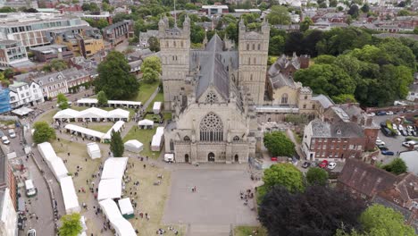 Aerial-view-of-Exeter-City-Cathedral-surrounded-by-bustling-market-stalls,-showcasing-historical-grandeur-in-Exeter,-Devon,-UK,-July-2024