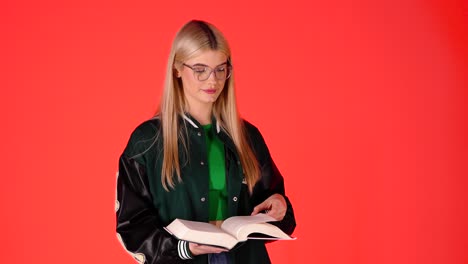 Estudiante-Bastante-Rubia-Leyendo-Un-Libro,-Voltea-Una-Página-Y-Mirando-La-Cámara,-Foto-De-Estudio-Con-Fondo-Rojo