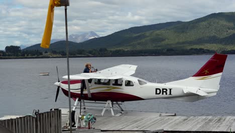 A-pilot-is-refilling-fuel-in-his-white-water-plane-on-an-island-in-New-Zealand-on-a-cloudy-day-with-mountains-in-the-background