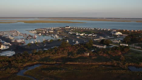 Harbor-and-parking-lot-full-with-boats-at-sunset-on-edge-of-wetlands-in-Chincoteague-Island-Virginia,-slow-motion