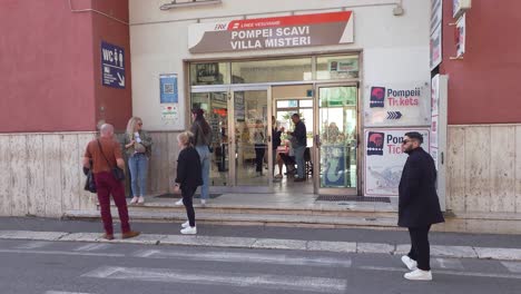 People-waiting-at-Pompeii-railway-station-with-sign-to-ticket-office---Naples,-Italy