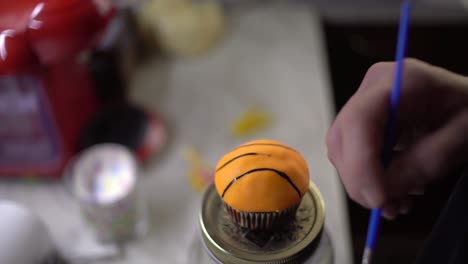 Close-up-on-woman's-hands,-painting-a-cupcake-as-a-basket-ball,-with-blurred-background,-static-4k-shot