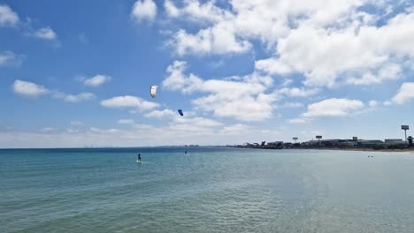 General-shot-of-people-kitesurfing-with-hydrofoil-on-a-blue-sea-beach-on-a-sunny-day-with-the-city-in-the-background