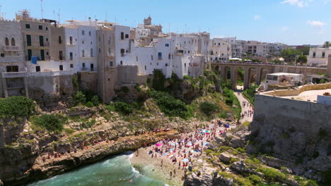 Multitud-De-Personas-En-La-Hermosa-Playa-De-Lama-Monachile-En-Polignano-A-Mare,-Bari,-Puglia,-Italia---Disparo-De-Drone