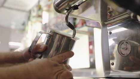 Milk-being-steamed-into-a-stainless-steel-container-with-an-espresso-machine-in-a-cafe