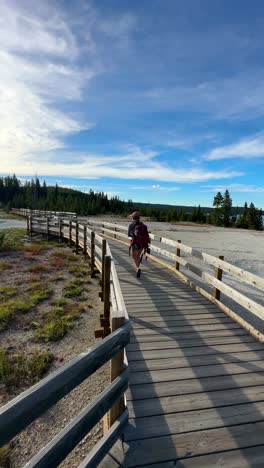 Vertikale-4K-Ansicht-Einer-Touristin-Mit-Rucksack,-Die-Auf-Einem-Holzpfad-Im-Yellowstone-Nationalpark-In-Den-USA-Läuft