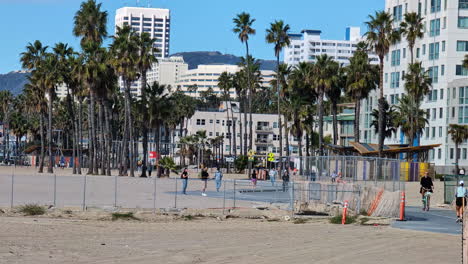 Vista-En-Cámara-Lenta-En-Un-Sendero-Peatonal-En-La-Playa-De-Arena-De-Los-Ángeles,-Gente-Pasando,-Bicicletas,-Corredores,-Día-Soleado