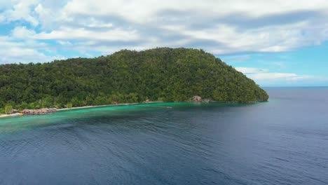 Plataforma-Aérea-Y-Toma-Inclinada-Hacia-Abajo-De-Una-Verde-Isla-Kri-En-El-Archipiélago-De-Raja-Ampat,-Indonesia,-Con-Un-Denso-Follaje-Que-Se-Encuentra-Con-El-Océano-Claro-Y-Turquesa